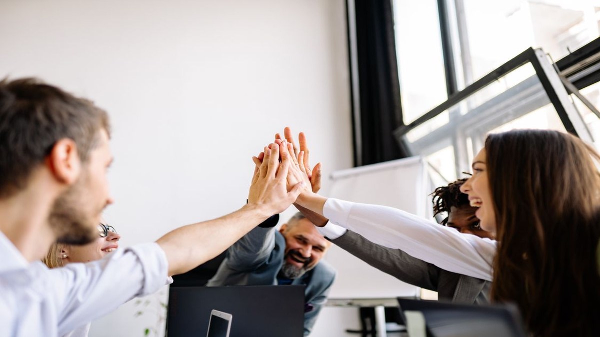 Diverse team doing a group high-five in a bright meeting room